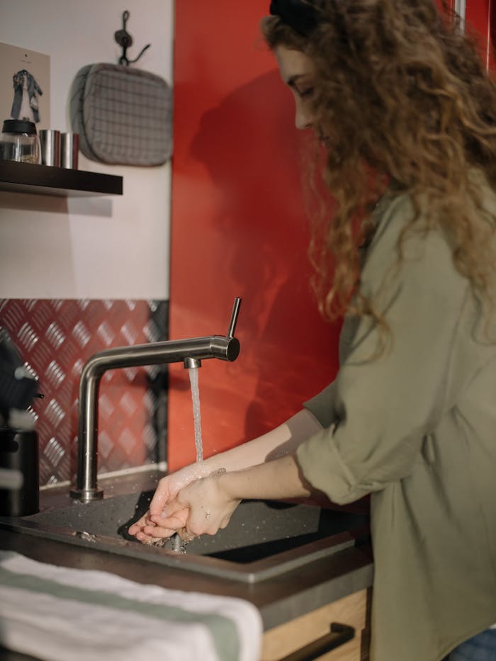 A woman washing her hands in a modern kitchen with a red accent wall.